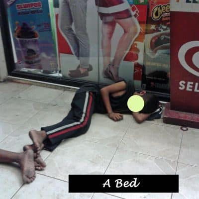 A young boy sleeping in relative safety outside a store.