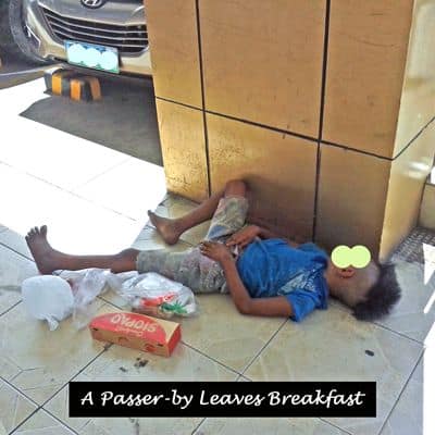 A passerby leaves breakfast for a young boy asleep on the pavement outside a store.