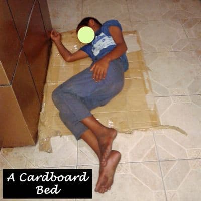 A young boy using cardboard as a bed as he sleeps in relative safety outside a store.