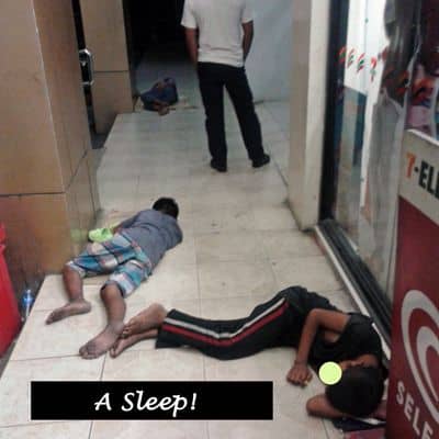 Young boys sleeping on the pavement outside a store.