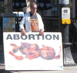 Man demonstrating against Abortion and holding placard with images of torn parts of aborted child.