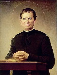 Image of St John Bosco standing behind a table.